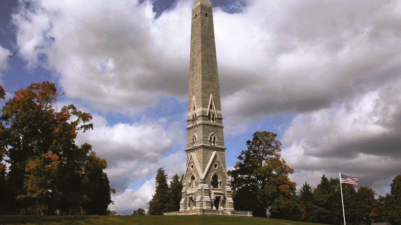 A partly cloudy sky behind a tall, gray obelisk monument