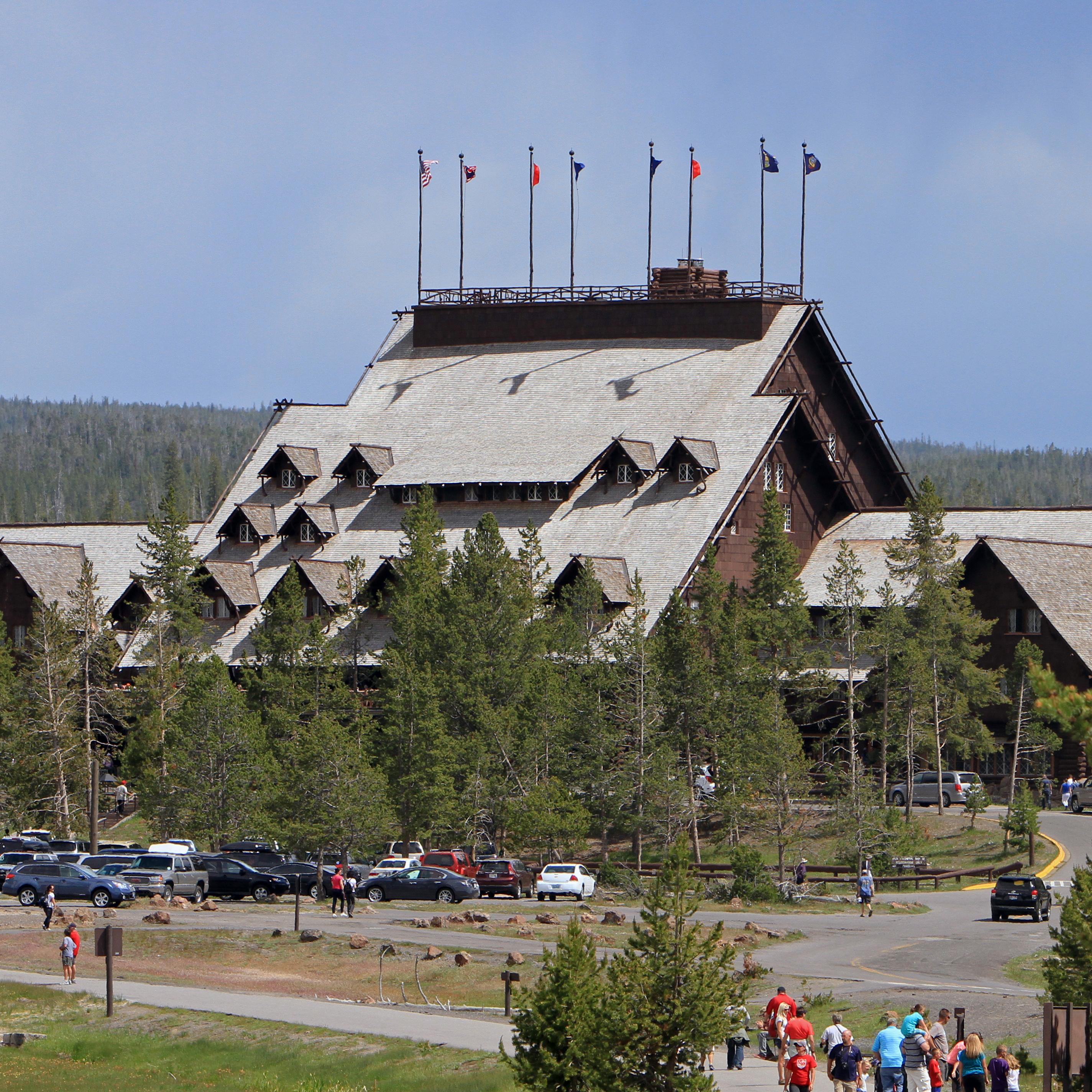 A large wooden building with a steep roof, trees, cars, and people in the front.