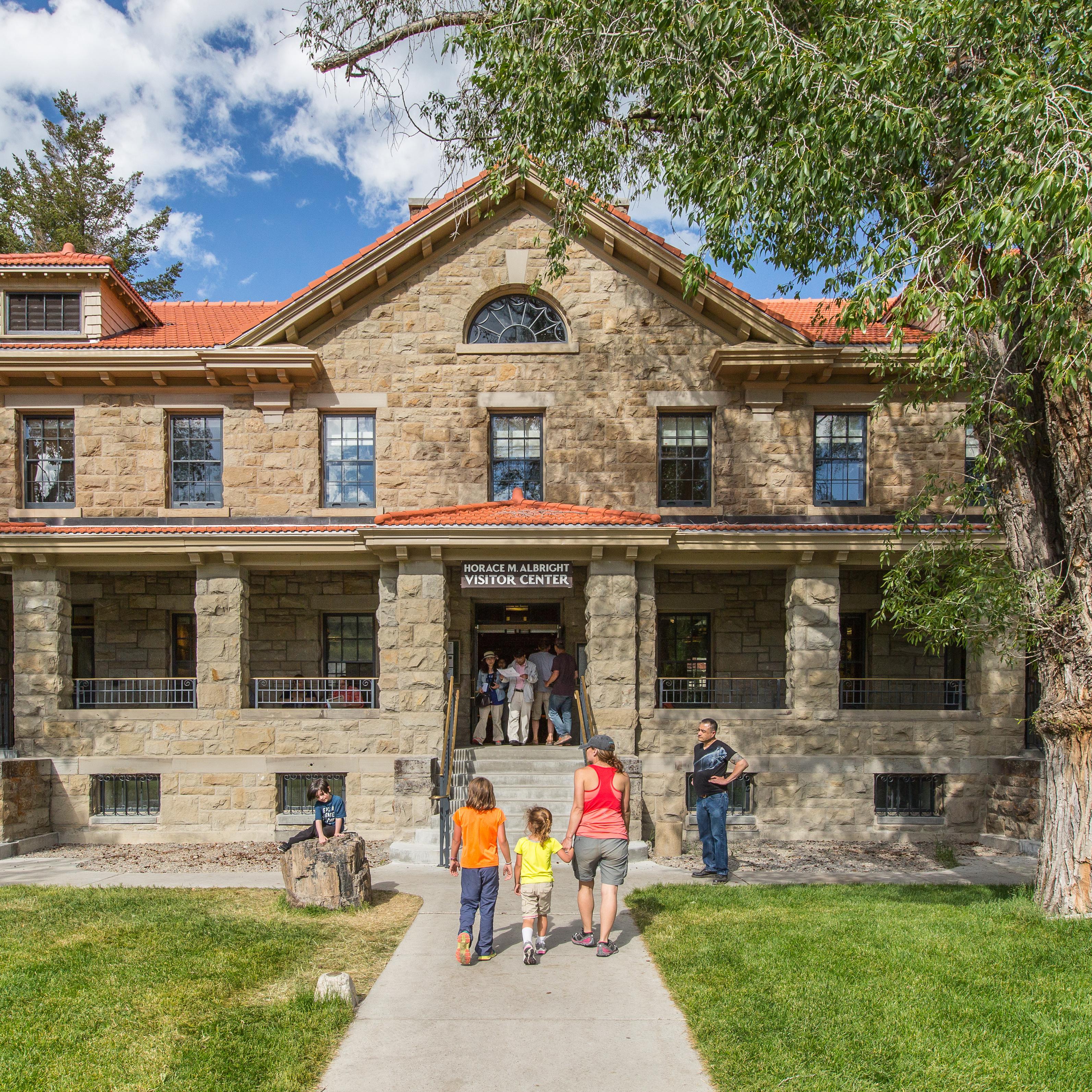 A stone building with large covered porch and red roof; people entering and exiting.