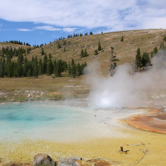 Steam rises from a blue-, yellow- and orange-colored hot spring.