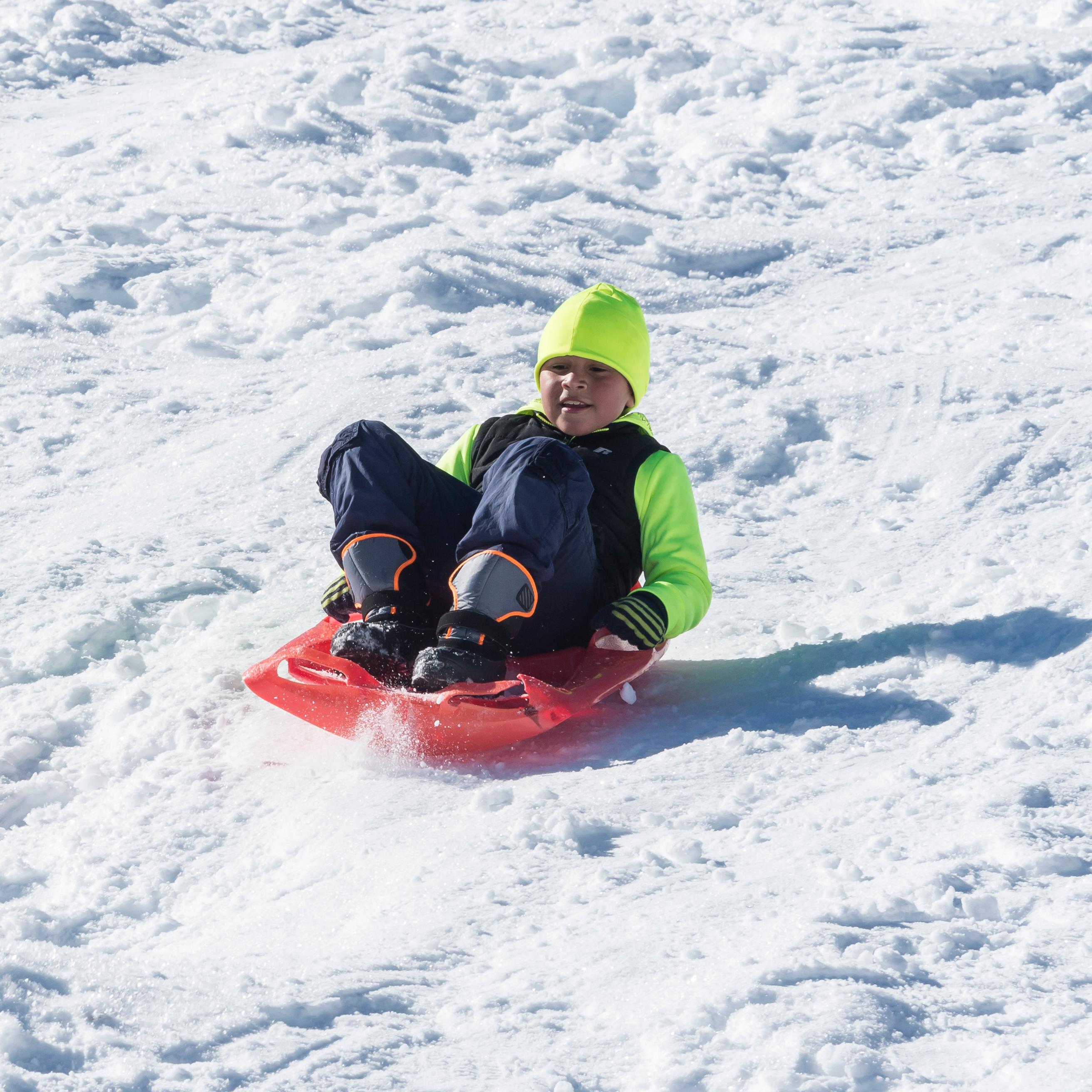 A young boy sleds down a snowy hill.