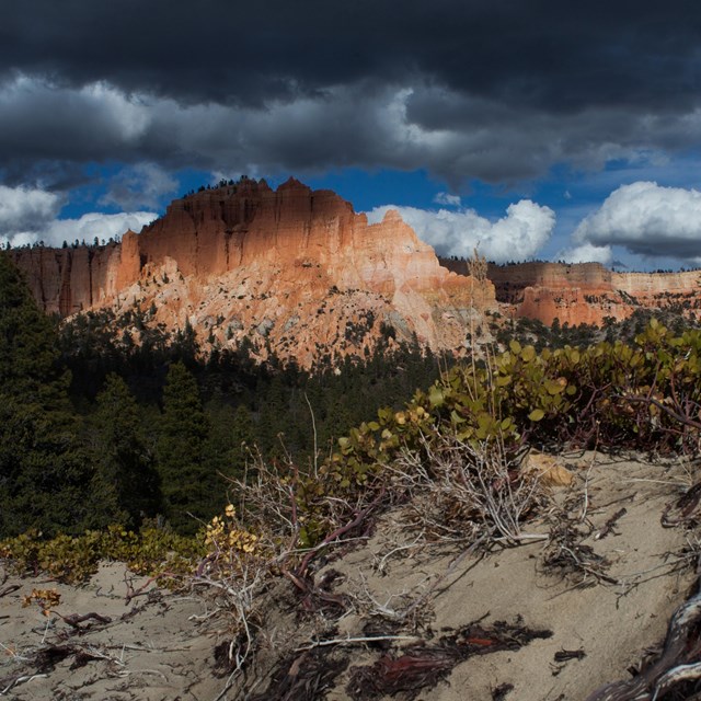 A large land formation with irregular red rock structures under dark storm clouds.