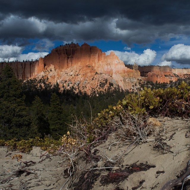 A large land formation with irregular red rock structures under dark storm clouds.