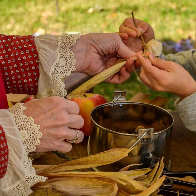 A close up picture of people making a cornhusk doll.