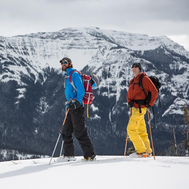 Two backcountry skiers look onward with mountain views in the background.