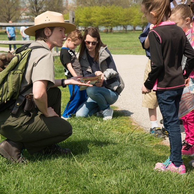 A park ranger crouched down talking to a group of children.