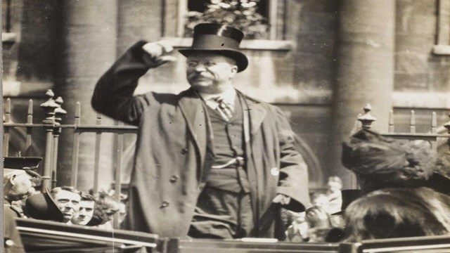 TR standing up in back of car, greeting crowd