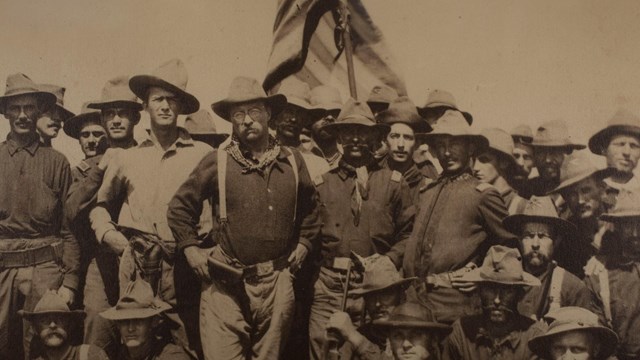 Theodore Roosevelt is posing with a crowd of his "Rough Riders" 
