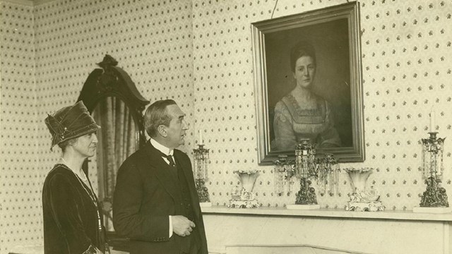 sepia photograph of two visitors in the birthplace admiring a portrait of TR's mother