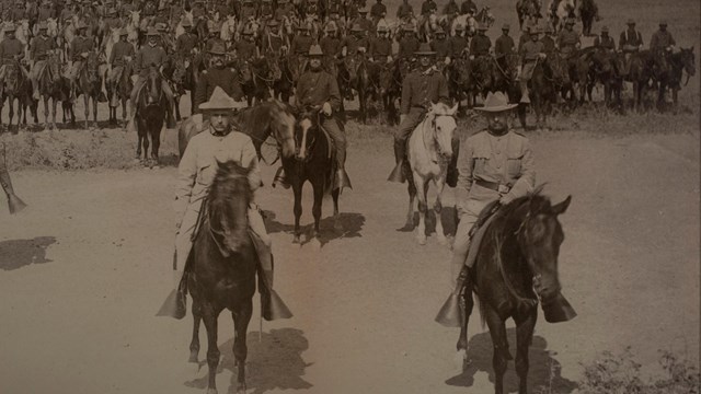 Sepia picture of TR on horseback in formation with other men riding horseback