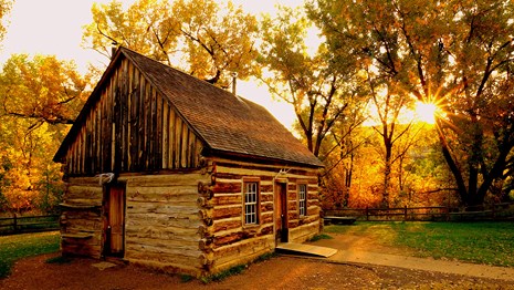 A rustic cabin in the yellow light of a rising sun.