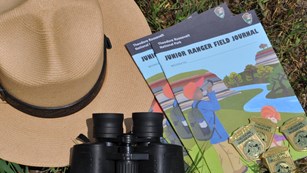 Ranger hat, binoculars, and Junior Ranger books and badges lying in grass.