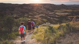 A family descends a dirt trail down into a rugged, green canyon.