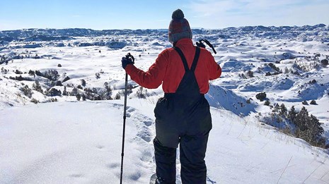 A person on snowshoes leaves tracks in the snow while descending a snowy hill into the badlands.