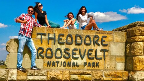 A smiling family sits atop Theodore Roosevelt National Park's stone entrance sign