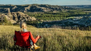 A person sits in a camp chair on the prairie overlooking the badlands