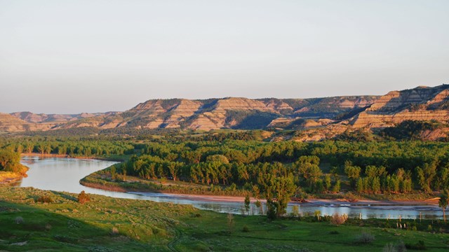 A view of the Little Missouri River with buttes and trees in the background.