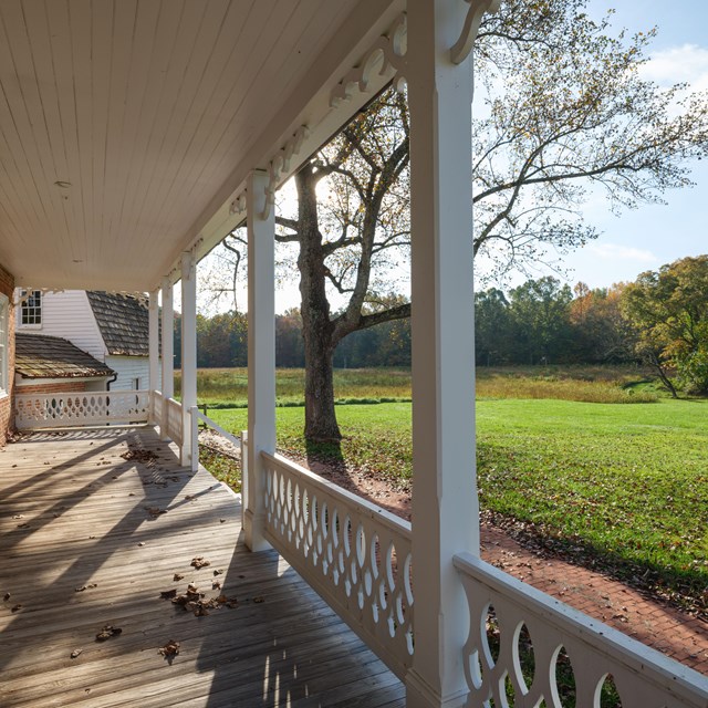 A deck with railing overlooking a green grass field and a blue sky.