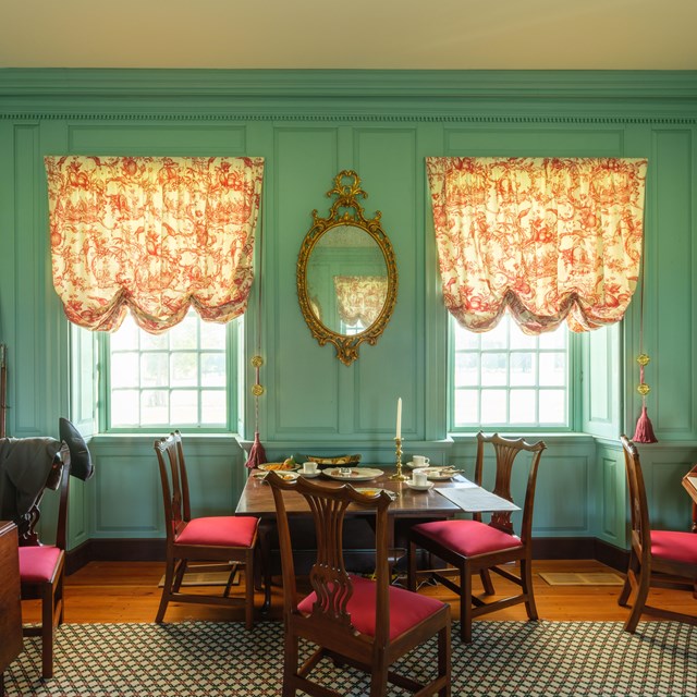 A colonial era office with green walls, large windows, and furniture.