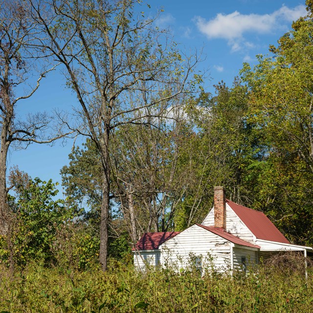 White tenant house with red roof, surrounded by vegetation and nature trail