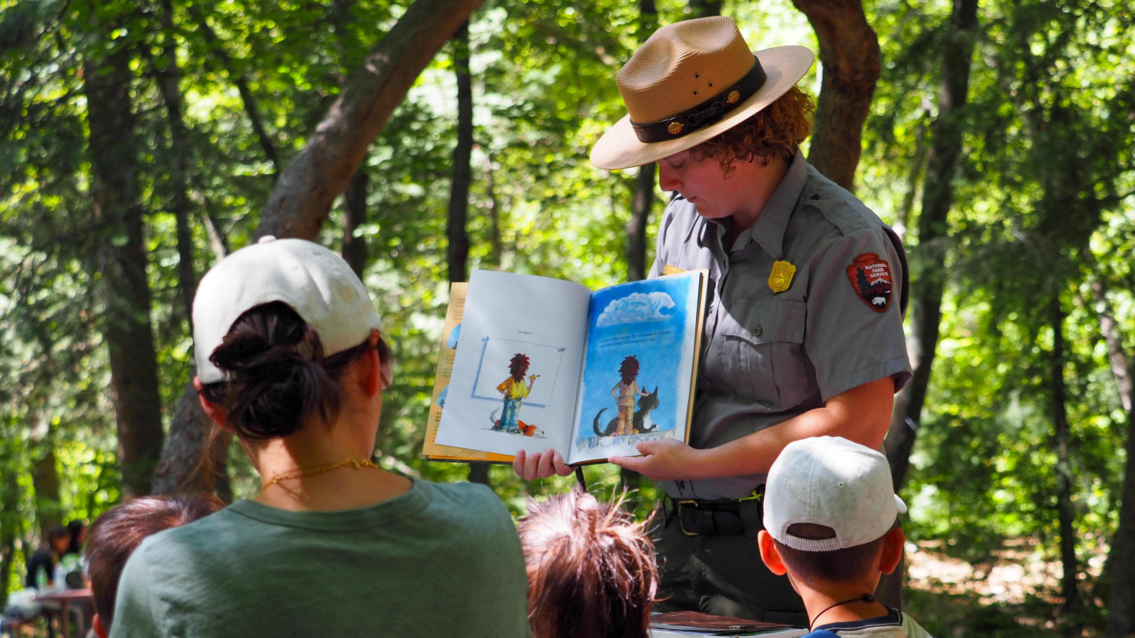 A ranger reading a picture book to a group of children.