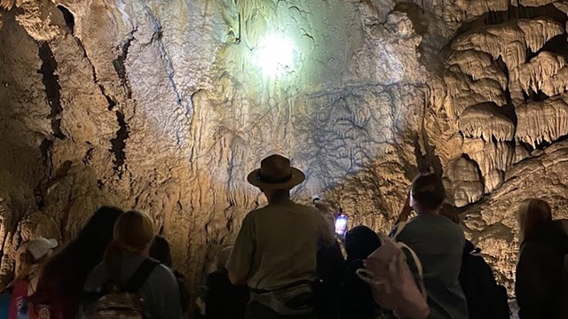A ranger leads a field trip group inside the cave. He shines a flashlight at tall flowstone.