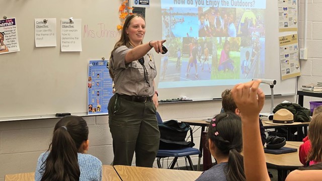 Ranger pointing at children with hands raised in a classroom