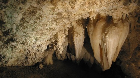 A large stalactite and other cave formations hang from the ceiling