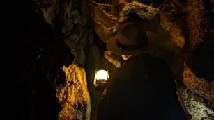 Ranger holding a lantern, illuminating decorated cave walls.