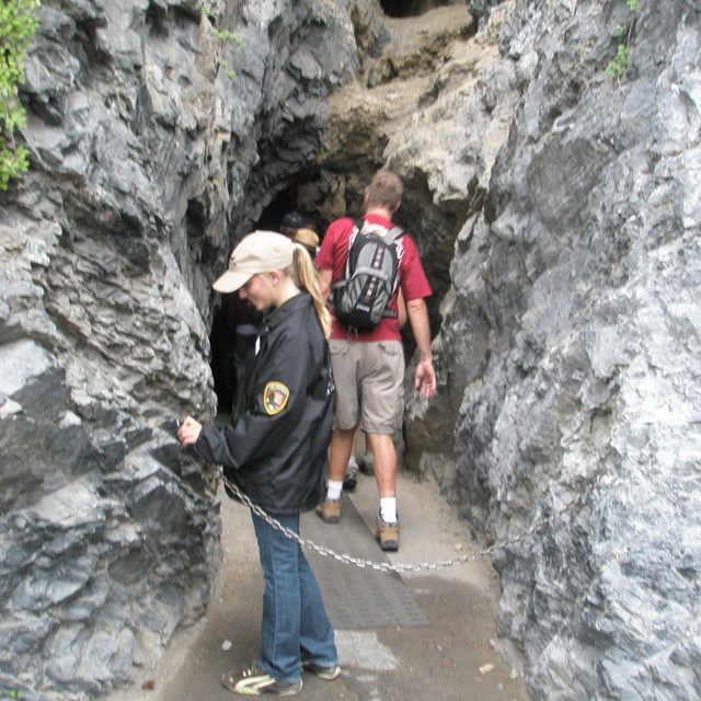 Youth volunteer securing chain and leading group of people into cave