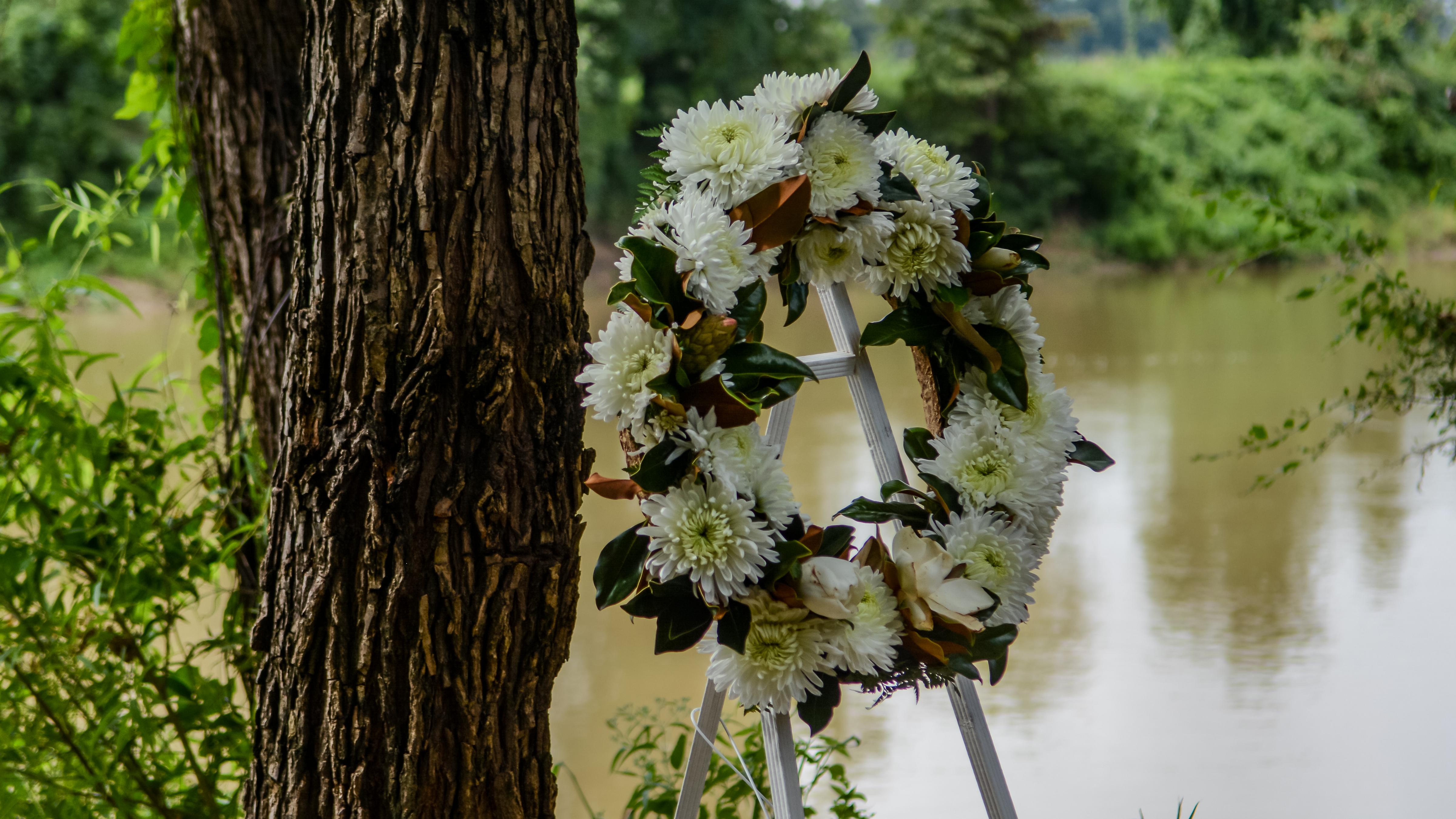 A floral wreath on a stand infront of a muddy river