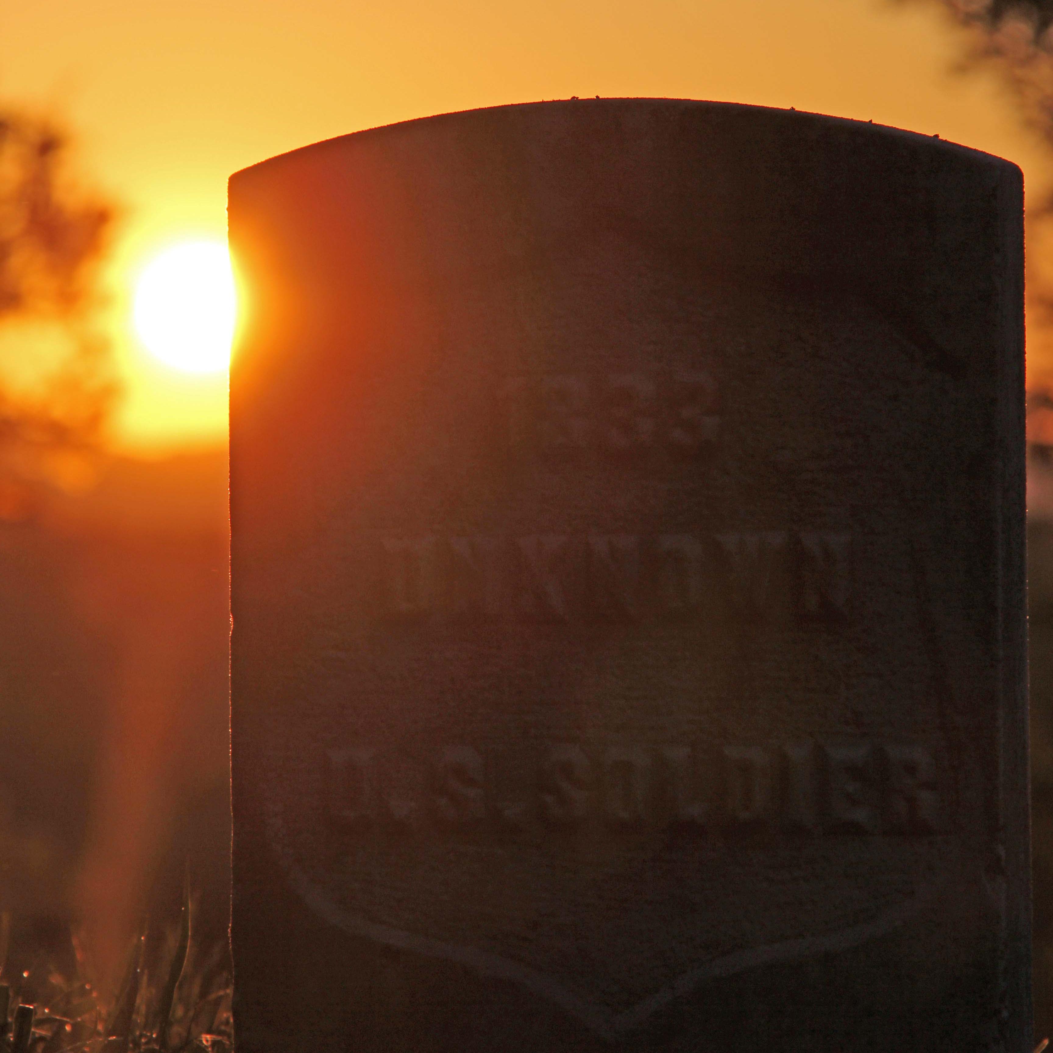A gravestone is lit from behind by the setting sun