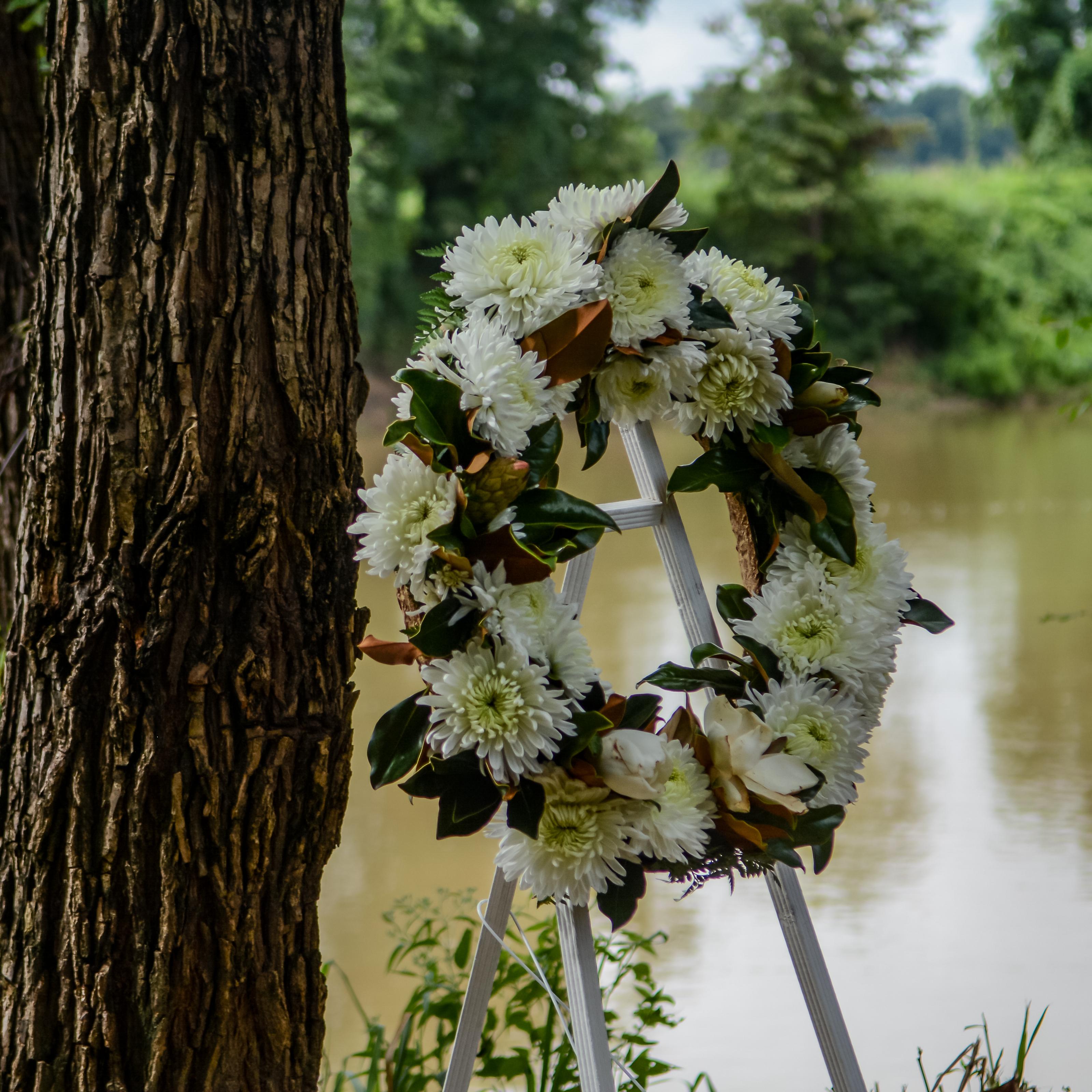 A floral wreath on a stand infront of a muddy river