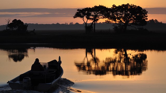 a boat at sunrise with an island featuring trees in the background