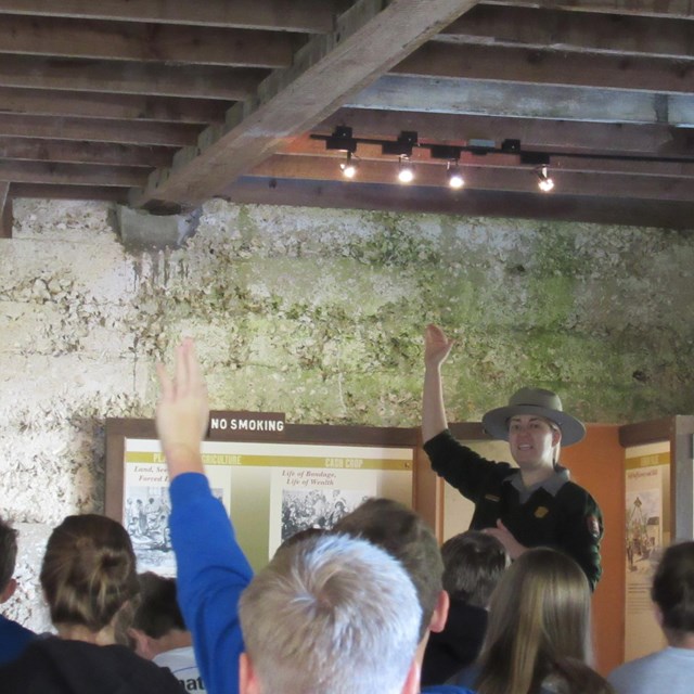 a ranger points to a slave cabin while school children follow