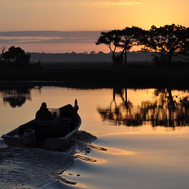 a boat at sunrise with an island featuring trees in the background