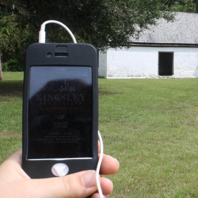 an audio tour device held by hand with historic barn in distance