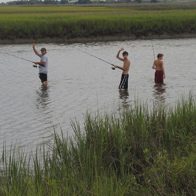three people stand in waist deep water fishing 