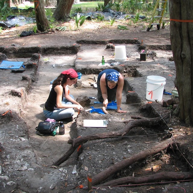 students in perfectly dug rectangular holes at a dig site 