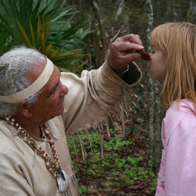 a living historian dressed as a Timucua applies face paint to a kid