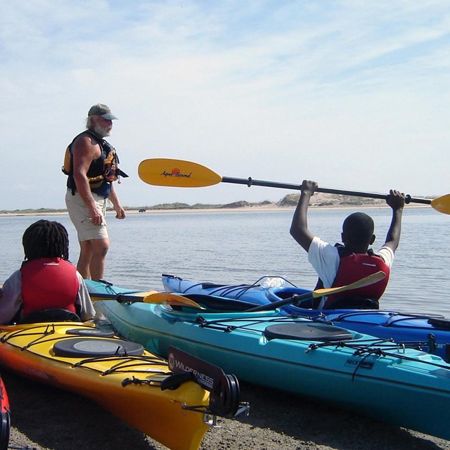 youth in kayaks on the beach with instructor at waters edge