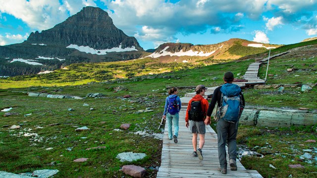 Three hikers hike on a boardwalk with a mountain in the distance.