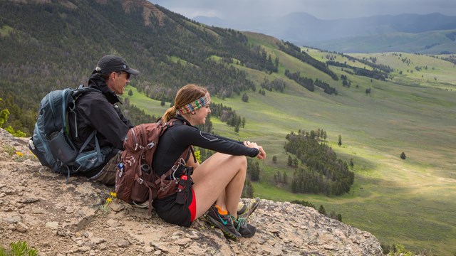 Two people sit on a rock looking at rolling green hills.