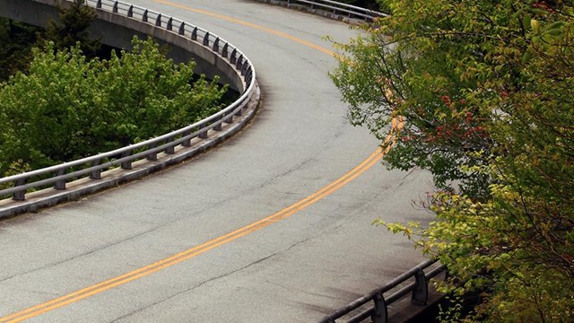 a road curves along side of a forested mountain