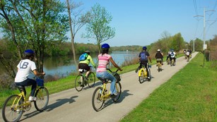 a group of young people biking on a bike path next to a body of water