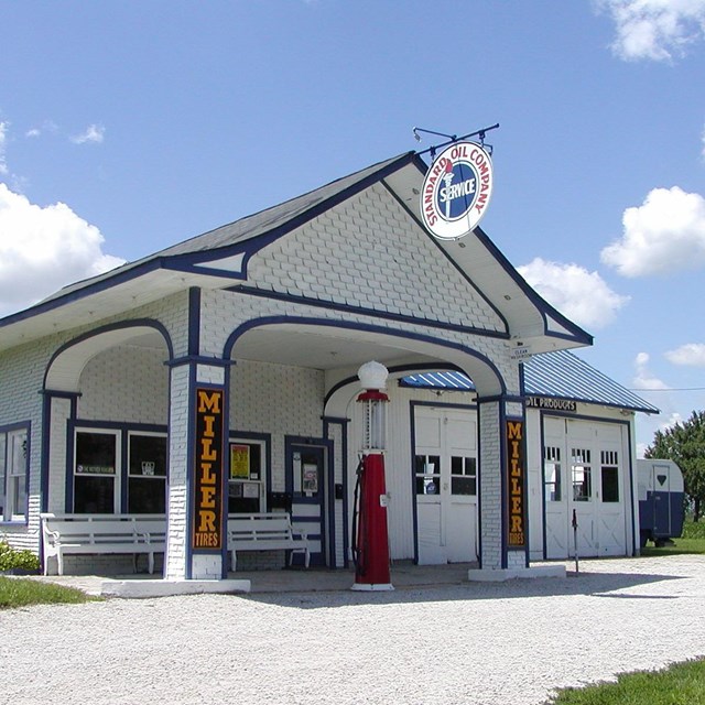A white, wood, single room historic gas station under a blue sky.