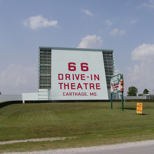 A large drive in theater screen with green grass in front.