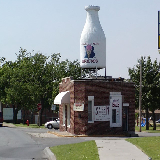 A small brick building with a giant milk bottle statue behind it.