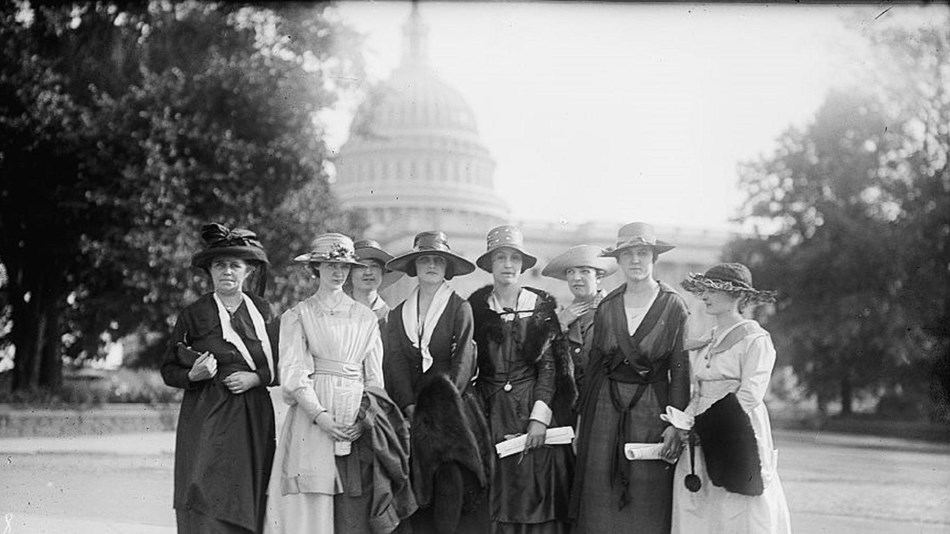 Group of women in early 20th century closing standing in front of Capitol Building.