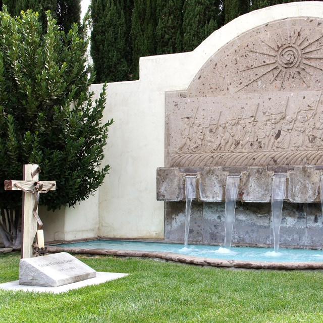 Stone cross on left in front of fountain and small pool. NPS photo. 